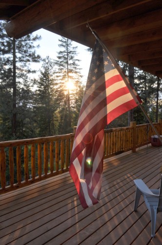Flag over a log house deck, at sunset in Montana